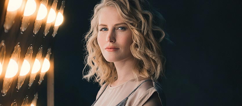 Blondes Model steht bei einem Fotoshooting neben einem Blitzlicht