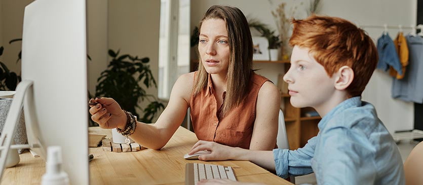 Frau gibt einem Schulkind Nachhilfe am PC